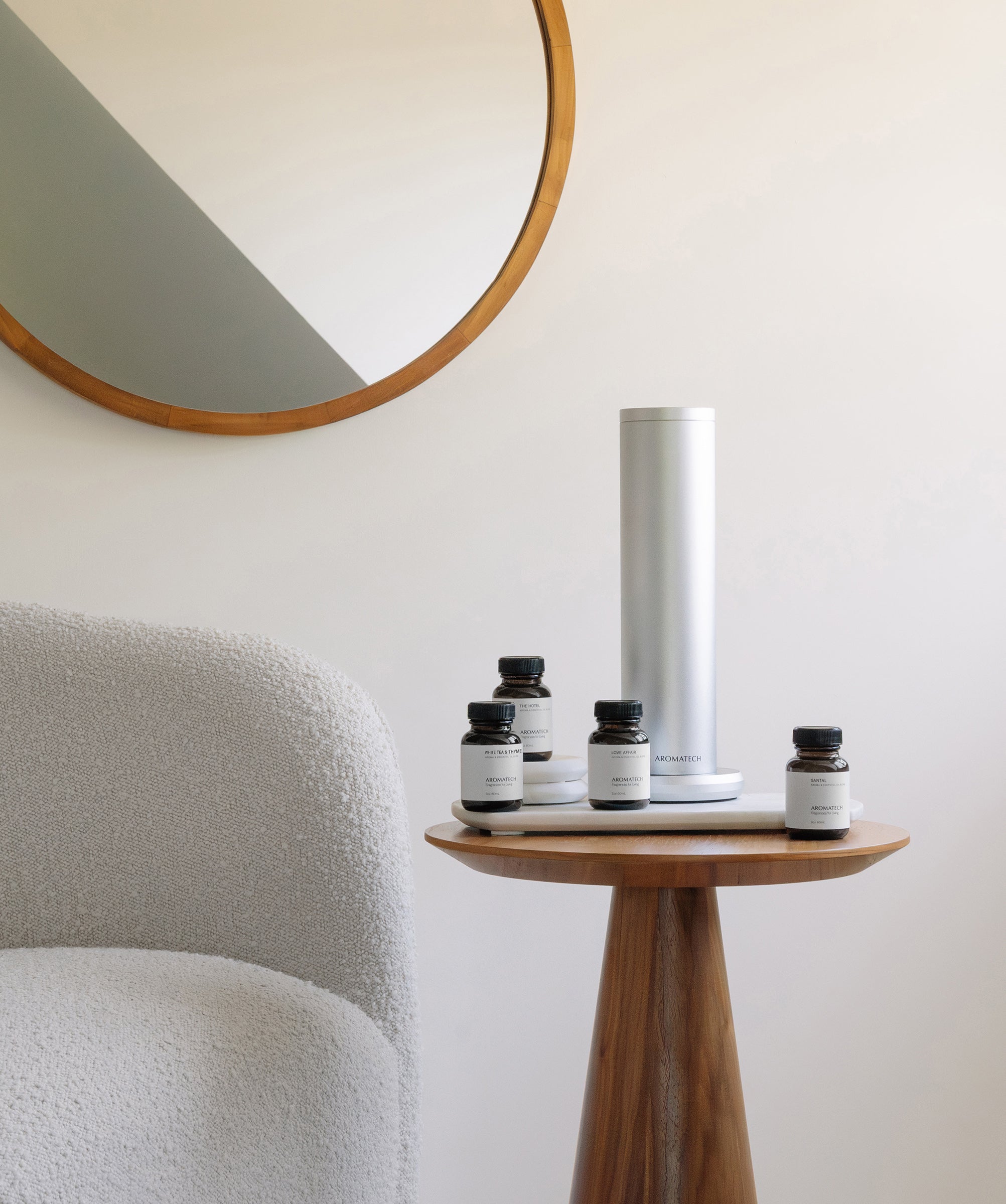 Silver AroMini BT Plus scent diffuser with fragrance oils on a wooden side table