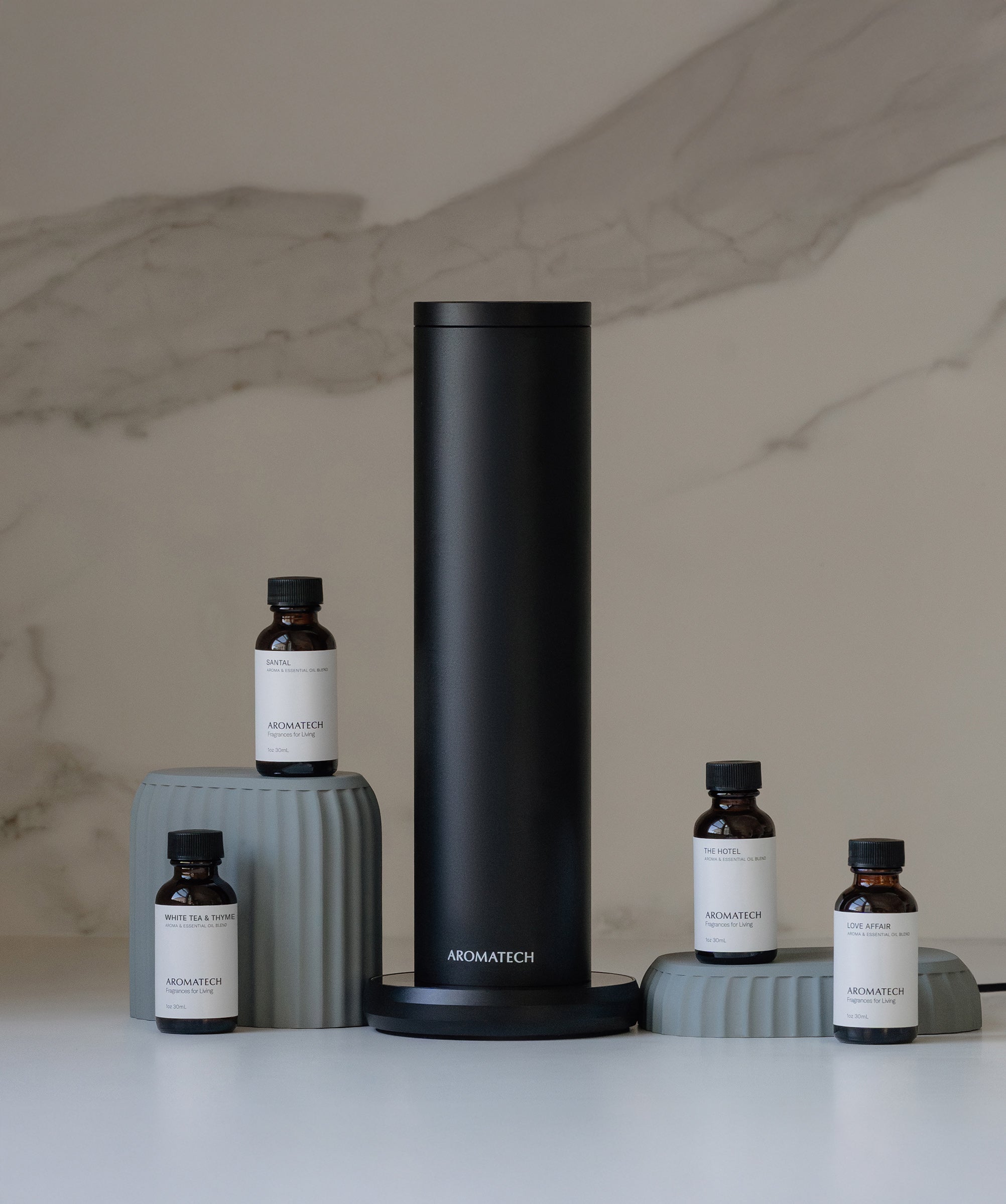 AroMini BT Plus scent diffuser with four fragrance oil bottles on a marble countertop